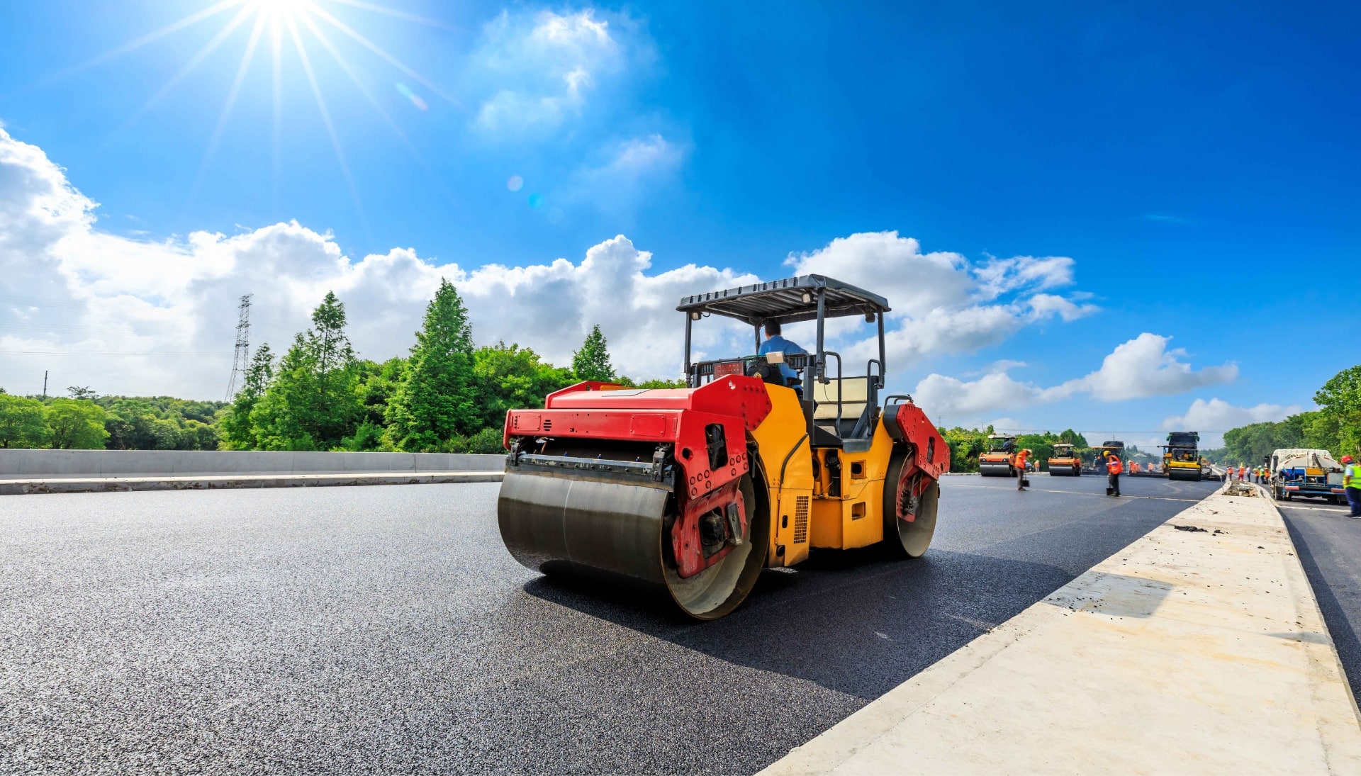 A team of construction workers operating heavy machinery, meticulously laying down fresh, smooth asphalt on a newly constructed road in Orlando, with steam rising from the hot surface.